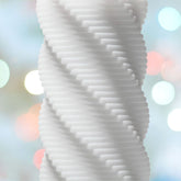 Close-up of a spiral, textured white column reminiscent of the Tenga 3D Spiral Penis Masturbator against a soft focus background with multicolored bokeh lights.
